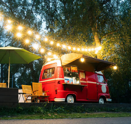 istockphoto-1420037836-612x612 Empty small Street Food Track with an illumination standing in the deserted night park. Near food trailer are folding tables and chairs